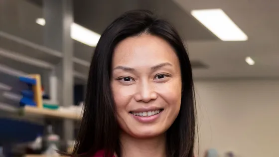 A smiling Asian woman with long black hair in an office environment.