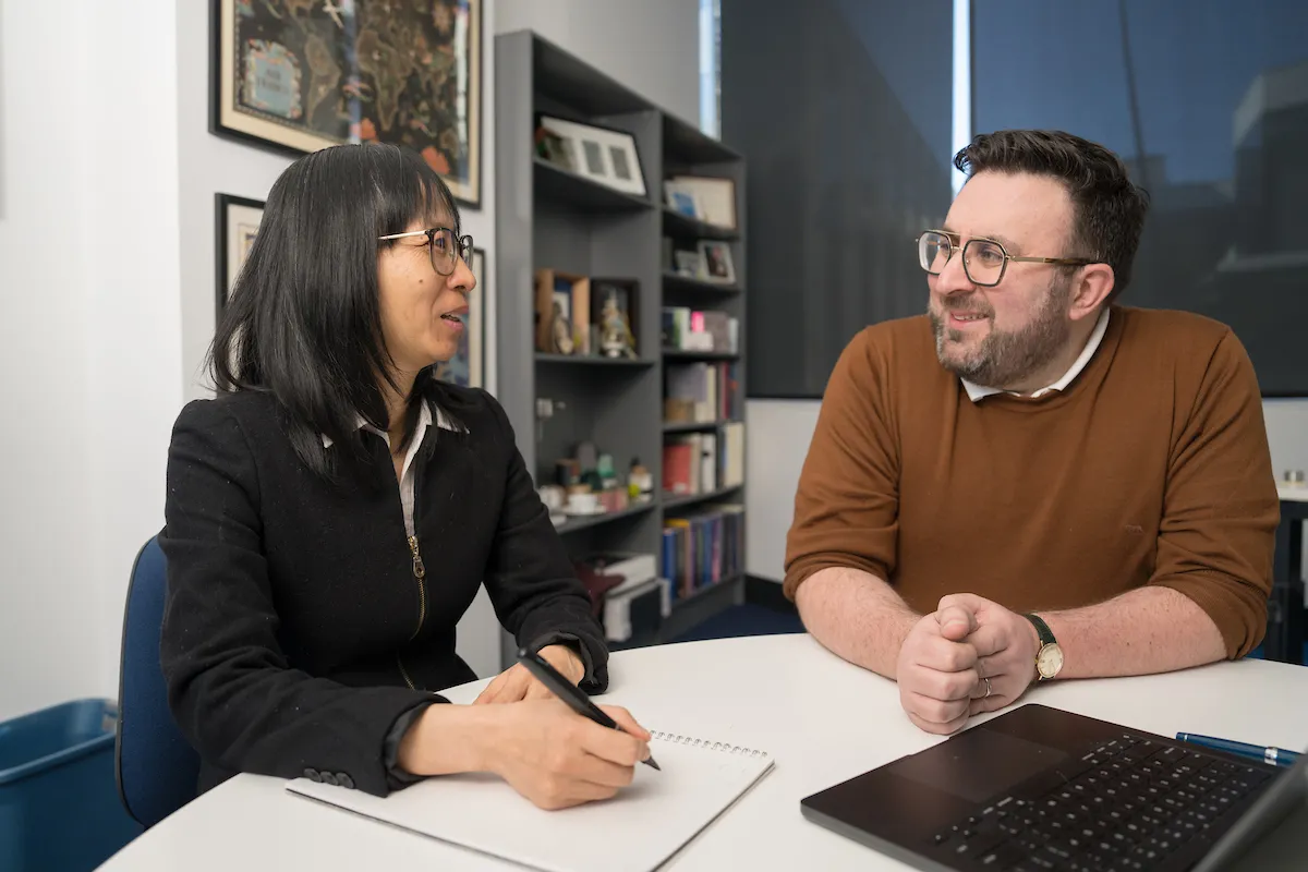 Nhung Nghiem and Mark Polizzotto are seated in an office and talking to each other..