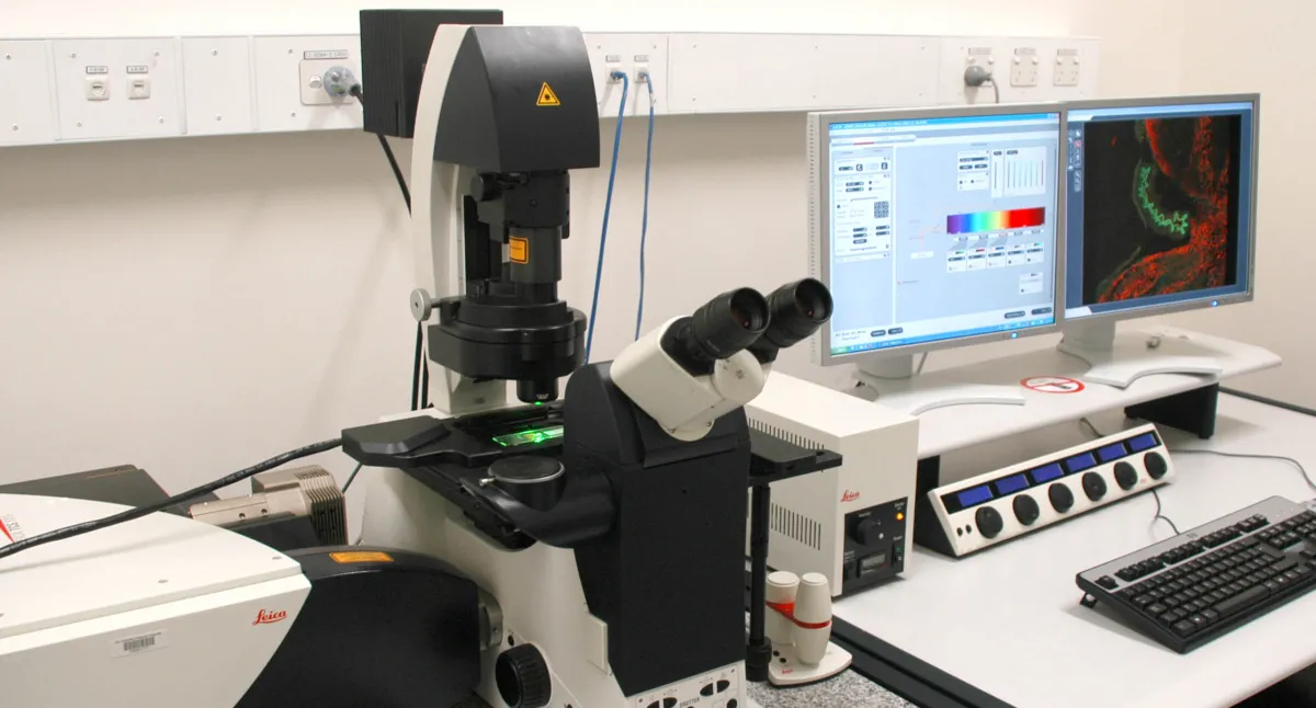 A modern laboratory setup featuring an advanced microscope linked to two computer monitors displaying scientific data.