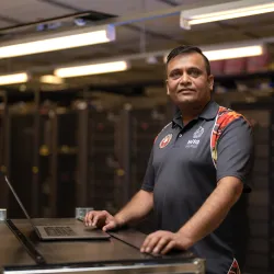 A man standing in a data center next to a laptop placed on a server rack, looking towards the camera.