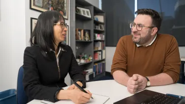 Nhung Nghiem and Mark Polizzotto are seated in an office and talking to each other..